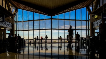  travelers standing in front of large window at airport